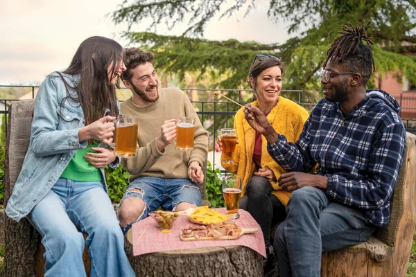Four Adults Sit Outdoors Tree Trunk Table Sharing Laughs Beers — Stock Photo, Image