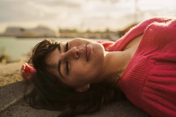 Moment of Peace - A young woman lies down near the harbor, eyes closed, basking in the sunlight. Her serene expression and the gentle coastal breeze evoke a feeling of pure relaxation and tranquility.
