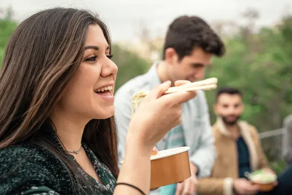 Woman Foreground Smiles She Savors Noodles Chopsticks Surrounded Friends Enjoying — Stock Photo, Image