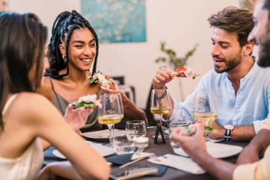 Bir grup arkadaş masanın etrafında şarap kadehleriyle kahkahalar ve güzel yiyecekler paylaşıyor, birlikte eğleniyorlar - pizza ve şarapla grup yemeği