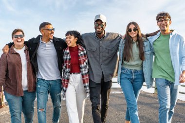 Bir grup genç, çeşitli arkadaş birlikte yürüyor ve gülüyor, birlik ve mutluluk sergiliyorlar..