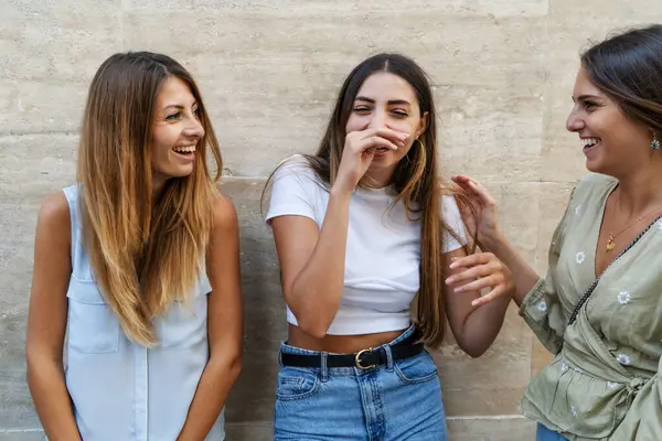 Three young women share a light-hearted moment, laughing and enjoying each other\'s company in a candid outdoor setting.