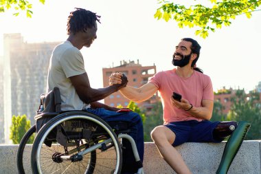 İki adam, biri protez bacaklı ve biri tekerlekli sandalyede, şehir dışında sıcak bir tokalaşma yaşıyor..