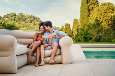 Romantik bir anı paylaşan çift havuz kenarında serinletici içecekler içiyor lüks bir tatil köyünde..