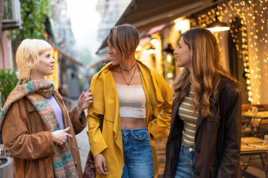 Üç arkadaş, sonbaharda huzurlu bir şehir ortamında rahatça yürüyüp kahkahalarını ve sohbetlerini paylaşıyorlar..