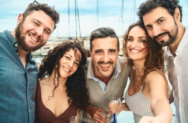 Bir grup neşeli arkadaş bir marinada kadeh kaldırırken selfie çekiyorlar. Arkadaşlığın ve kutlamanın neşesini somutlaştırıyorlar..