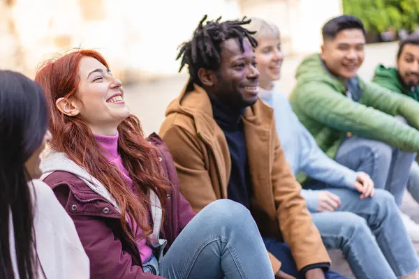 Laughing red-haired woman with diverse friends enjoying a casual outdoor meeting, embodying the joy of companionship.