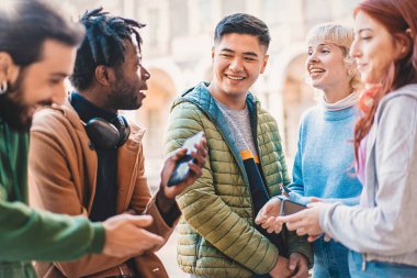 Kampüs avlusunda bir mola sırasında gülümseyen ve akıllı telefonlarla meşgul olan çeşitli üniversite öğrencileri..