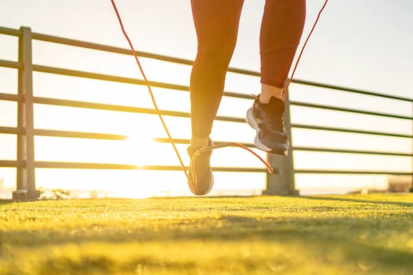 Silhouette of a woman jump roping during a vibrant sunrise, engaging in a morning cardio workout.