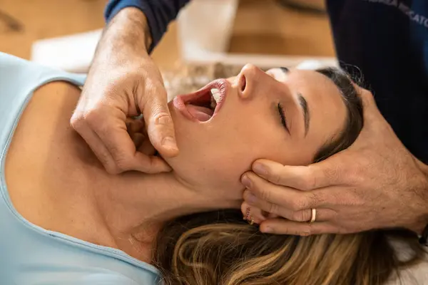 Bir osteopat, kadın bir hasta üzerinde çene ayarlaması yapar, gerginliği azaltmaya ve eklem işlevini geliştirmeye odaklanır.
