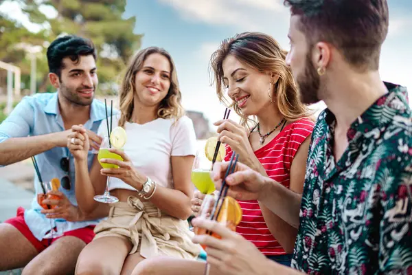 Group of friends sharing a laugh over cocktails at an outdoor summer meet-up.