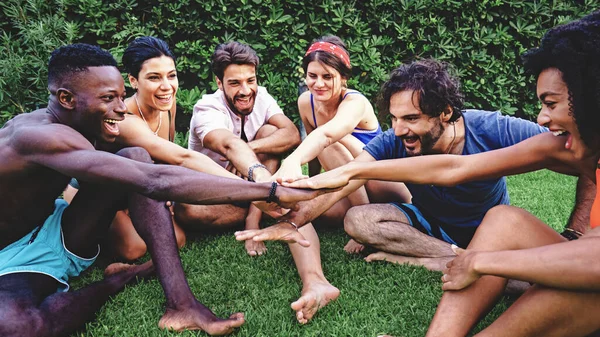 Group of multicultural friends laughing and enjoying a team-building game on a green lawn, sharing a moment of joy and unity.