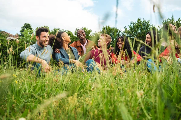 A diverse group of young people laughs and enjoys a relaxing moment, surrounded by lush greenery, highlighting the joy of friendship.