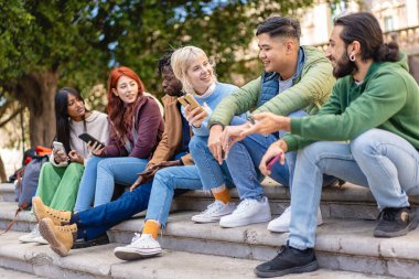 Çeşitli arkadaşlar akıllı telefonlardaki içerikleri paylaşır ve gülerler, şehir ortamında basamaklarda otururlar..