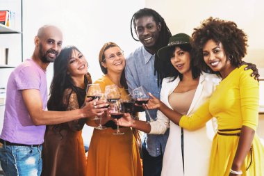 Kırmızı şarapla kadeh kaldıran neşeli çok ırklı arkadaşlar kapalı bir partide keyif ve dostluk bir grup kutlamasında gülümseme ve mutluluk.