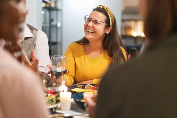 Woman in yellow laughing joyfully with friends during a casual dinner - Warm social gathering with food and drinks