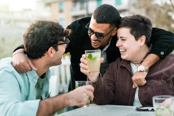 Casual outdoor drinks with diverse friends - Non-binary individual laughing and toasting drinks with friends at an outdoor gathering, showcasing joy and LGBTQ+ inclusivity