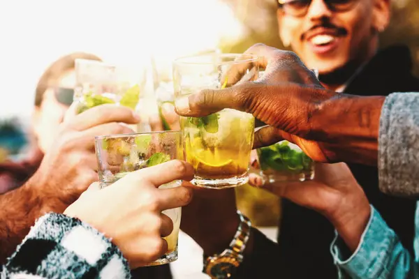 Multiracial friends clinking glasses of fresh mojito in a vibrant celebration - Happiness and refreshment at a social gathering.
