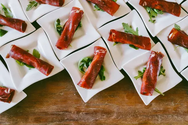 stock image Elegant presentation of meat appetizers on a bed of greens, arranged in small white square plates, showcasing gourmet appetizers in a visually appealing manner.