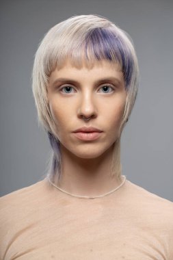 Sarı saçlı, mor röfleli septum piercingli ve şeffaf bluzlu genç bir kadının yakın plan portresi. Modern saç stili ve makyaj, moda endüstrisi, stüdyo fotoğrafları..