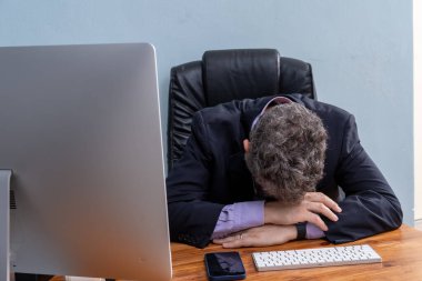 Profesyonel iş adamı, kafası bilgisayarın önünde dinlenirken yorgun. Şirket stresi, tükenmişlik ve zorlu bir çalışma ortamının zorlukları..