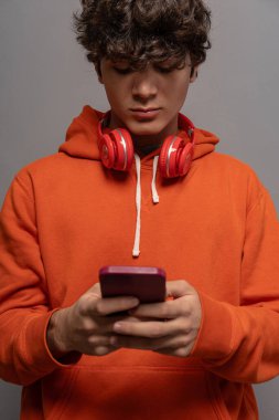 Teenager wearing an orange hoodie and red headphones using a smartphone, casual fashion, modern youth, technology, focus on device, isolated background clipart