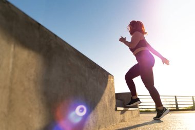 Geniş ölçekli bir kadın açık hava egzersizi sırasında mercek ışığı efekti, azim ve zindelik motivasyonu, sağlıklı yaşam tarzı, parlak ve güneşli bir gün, aktif ve dinamik hareket