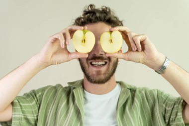 Gülümseyen ve gözlerinin üzerinde elma dilimleri tutan bir adam, neşeli ve sağlıklı bir portre oluşturuyor. Sağlık, yaratıcılık ve neşeli anlar hakkında içerik için ideal.