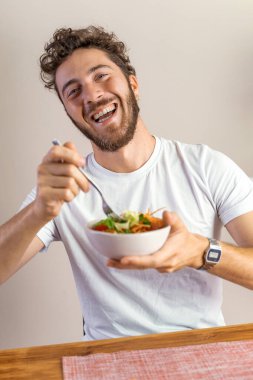 Sağlıklı salatanın tadını çıkaran gülümseyen bir adam. Beslenme, sağlıklı beslenme ve keyifli yemek deneyimleri için idealdir..