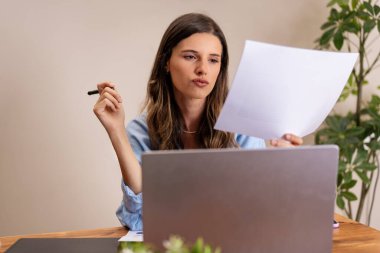 Ofisteki masasında belgeleri inceleyen odaklanmış bir kadın. Profesyonel ve konsantre - uzaktan çalışma, belge analizi, modern ev ofisi, verimlilik sahnesi.