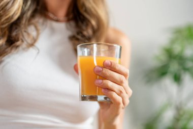 Elinde bir bardak portakal suyu tutan bir kadın, sağlıklı içecekler ve taze meyve suyu seçenekleri sunuyor. Sağlıklı içecek - ferahlatıcı, içkili kadın, beslenme.