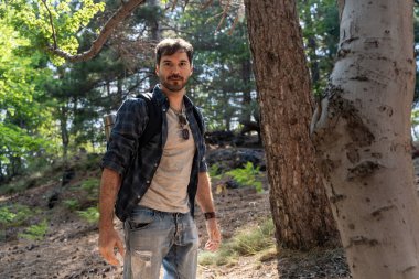 Kendine güvenen erkek yürüyüşçü yemyeşil orman patikalarını keşfeder. Günlük kıyafetli, sakallı maceraperest orman yürüyüşünün tadını çıkarıyor. Açık hava yaşam tarzı ve doğa bağlantısı kavramı.