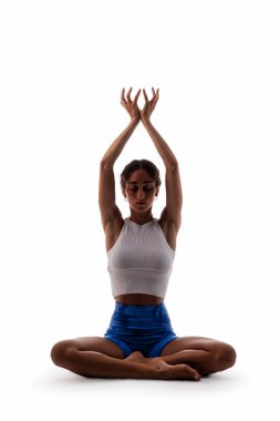 Siyahi bir kadın meditasyoncu yoga pozu veriyor, kolları havada lotus pozisyonunda oturuyor. Beyaz arka planda farkındalık, denge ve iç huzuru gösteriyor.