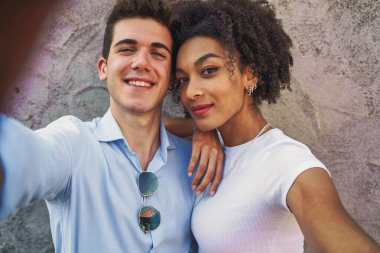 Genç, çok kültürlü bir çift selfie çekerken romantik bir anı paylaşıyorlar. Kentsel bir ortamda çeşitlilik, modern ilişkiler ve neşeli bağlar sergiliyor.
