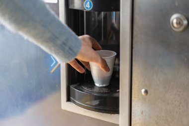 Otomatik otomatikman kahve dolu tek kullanımlık bir fincana uzanan birinin eline yakın çekim. İş yerinde veya kamusal alanda modern kolaylık, hızlı ferahlatıcı konsept.