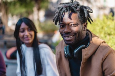 Uzun siyah saçlı, gülümseyen bir kadınla birlikte kulaklık takan neşeli bir Afrikalı adamın portresi. Farklı çiftler şehir merkezinin tadını çıkarıyorlar - arkadaşlık ve kapsayıcılık..