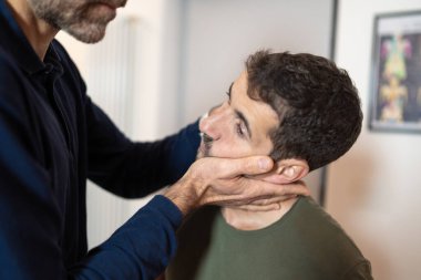 Servikal manipülasyon ve temporomandibular eklem (TMJ) değerlendirmesi yapan bir osteopatın erkek hasta üzerinde yaptığı yakın çekim - boyun ve çene ağrısı için elle tedavi tekniğini uygula.