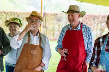 Bir grup aktif son sınıf öğrencisi açık hava barbeküsünde şarap içiyor. Önlüklü ve şapkalı yaşlı arkadaşlar yaz barbekü partisinde sosyalleşiyorlar ve içiyorlar..