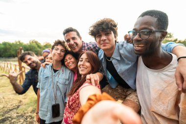 Mutlu çok kültürlü arkadaş grubu parkta selfie çekiyor. Genç ve çeşitli insanlar yaz tatili boyunca arkadaşlığın tadını çıkarıyorlar.