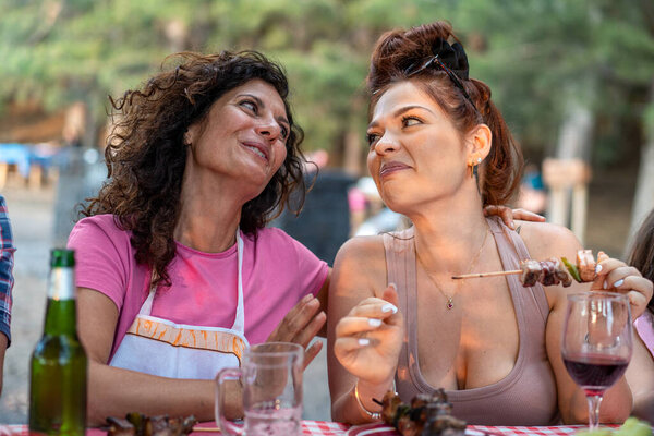 Multicultural female friends enjoying cheerful conversation during outdoor picnic. Natural candid moment of women sharing laughter and food at summer gathering