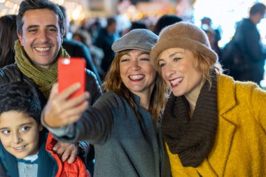 Mutlu aile Noel pazarında akıllı telefon özçekimi ile neşeli anıları yakalıyor. Baba ve oğlu ve arkadaşları birlikte tatil atmosferinin tadını çıkarıyorlar - otantik çoklu jenerasyon anı - yaşam tarzı.