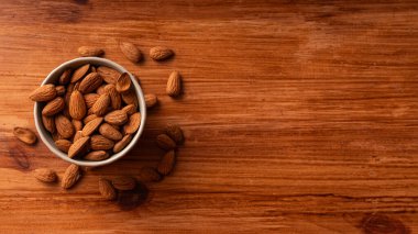 Beyaz seramik kâse içinde organik bademler kırsal ahşap masa zemininde fotokopi alanı ile