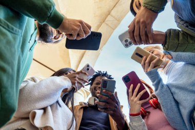 Açık havada akıllı telefonlar kullanan, sosyal medya içeriğini paylaşan çok ırklı bir grup genç arkadaş - çağdaş teknoloji yaşam tarzı kavramı