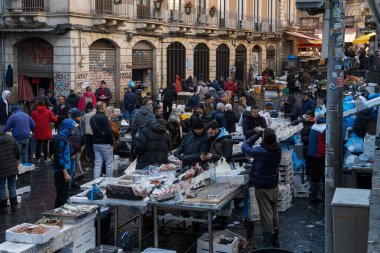 Catania, İtalya - 30 Aralık 2024: Catania, Sicilya 'daki tarihi balık pazarında canlı sahneler - satıcılar, müşteriler ve taze deniz ürünleri tezgahları. Sicilya geleneklerini yansıtan canlı bir kültür merkezi..