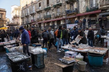 Catania, İtalya - 30 Aralık 2024: Catania, Sicilya 'daki tarihi balık pazarında canlı sahneler - satıcılar, müşteriler ve taze deniz ürünleri tezgahları. Sicilya geleneklerini yansıtan canlı bir kültür merkezi..