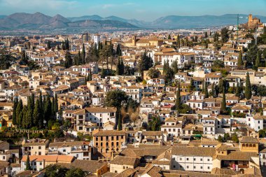 Granada, İspanya 'nın panoramik manzarası, geleneksel İspanyol mimarisi sergileniyor, kiremitli çatılar, ve berrak mavi gökyüzü altında manzaralı şehir manzarası.