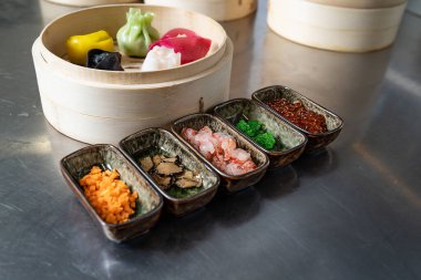 Bambu tenceresinde renkli mantı ve gurme malzemeler ve servis kaseleri.