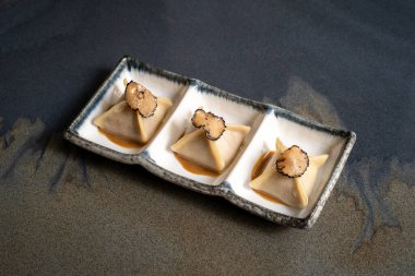 Three artisanal dumplings served in a white ceramic dish, topped with black truffle slices, showcasing gourmet culinary artistry. clipart