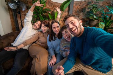 Bir grup genç arkadaş birlikte eğlenceli bir selfie çekiyorlar kapalı bir ortamda, neşeli ve neşeli bir anı yakalıyorlar..