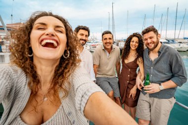 Bir grup neşeli arkadaş marinada bir teknede selfie çekiyorlar, yaz tatilinin tadını çıkarıyorlar ve arkadaşlığımızı kutluyorlar..